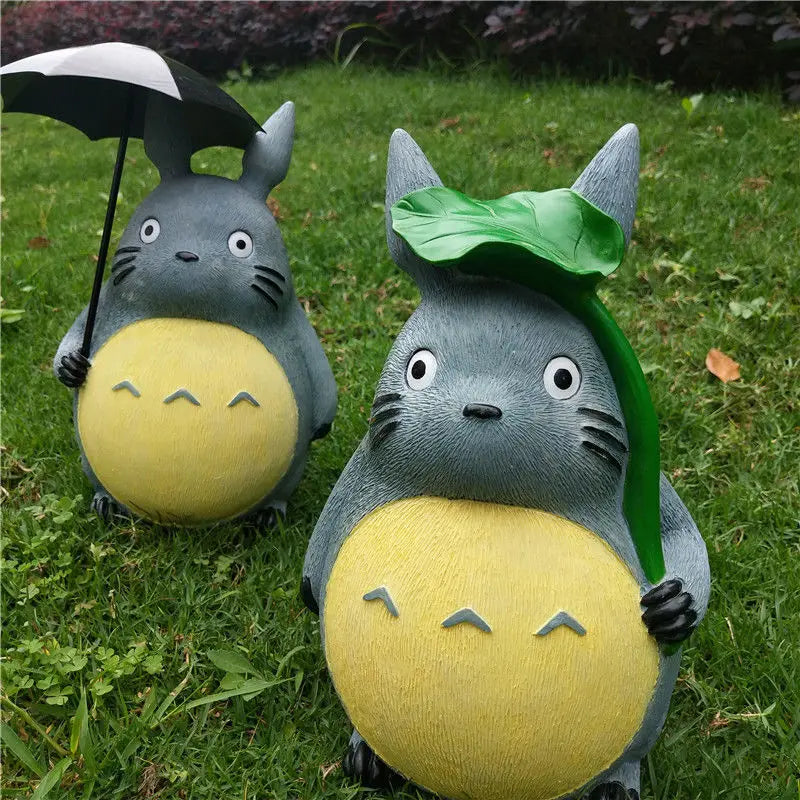 Two resin forest friend statues with leaf and umbrella accents displayed on a green lawn