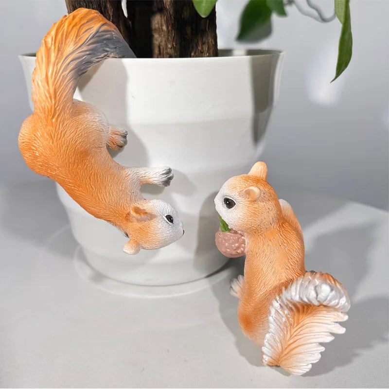 Two resin squirrel planter ornaments, one hanging from a pot, one standing nearby