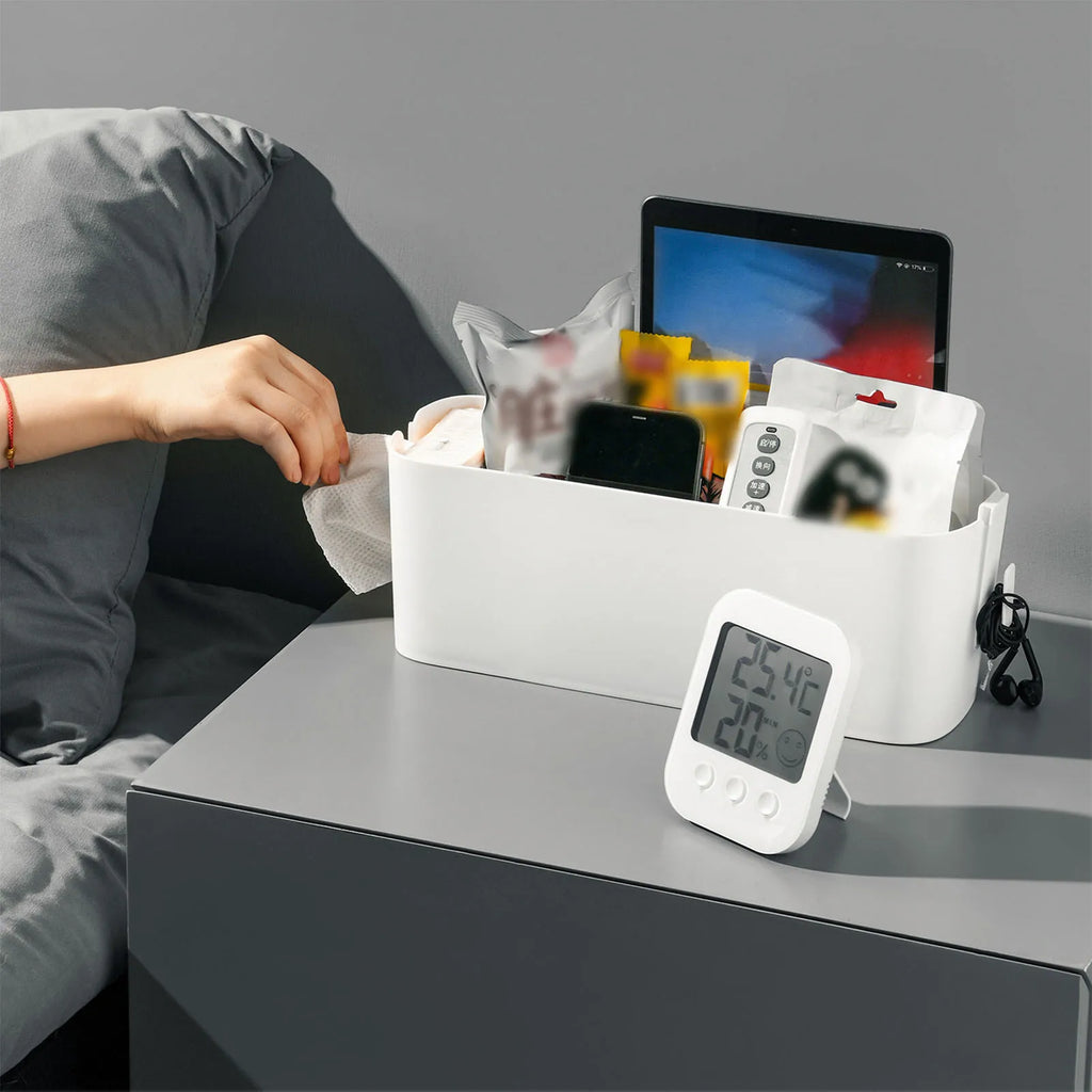 White bedside organizer basket filled with tablet, phone, remote, and other small items on a nightstand