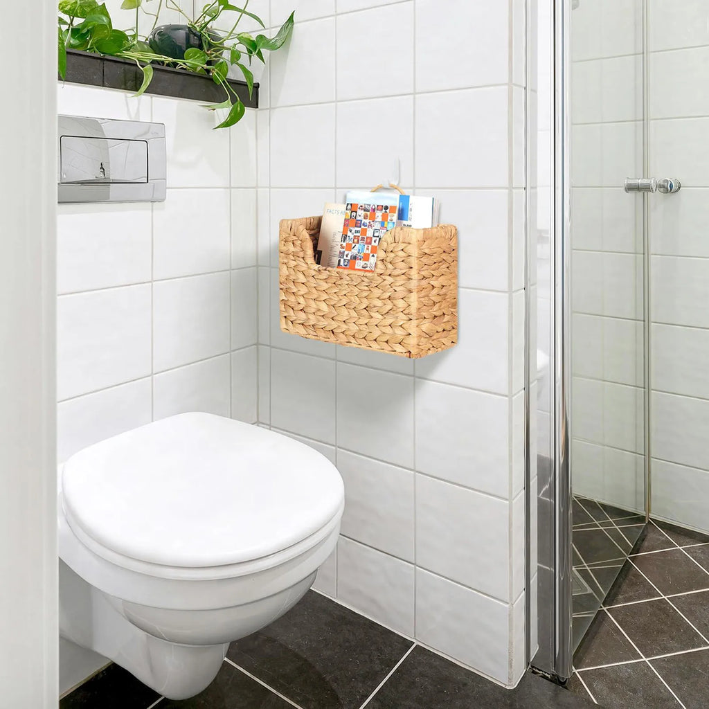 Woven magazine wall basket hanging above a toilet in a tiled bathroom, holding magazines and mail