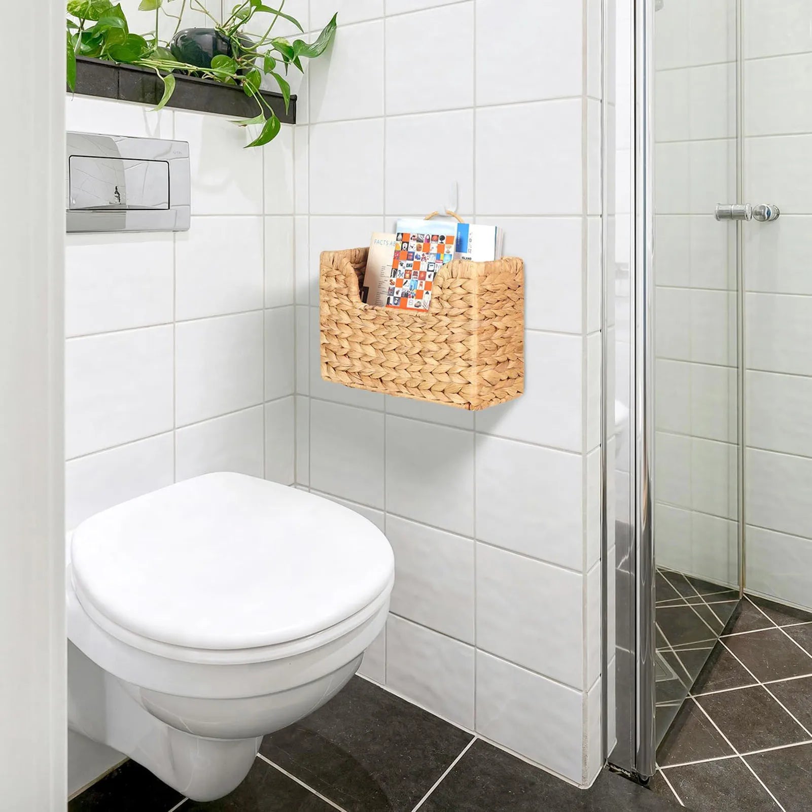 Woven magazine wall basket hanging above a toilet in a tiled bathroom, holding magazines and mail