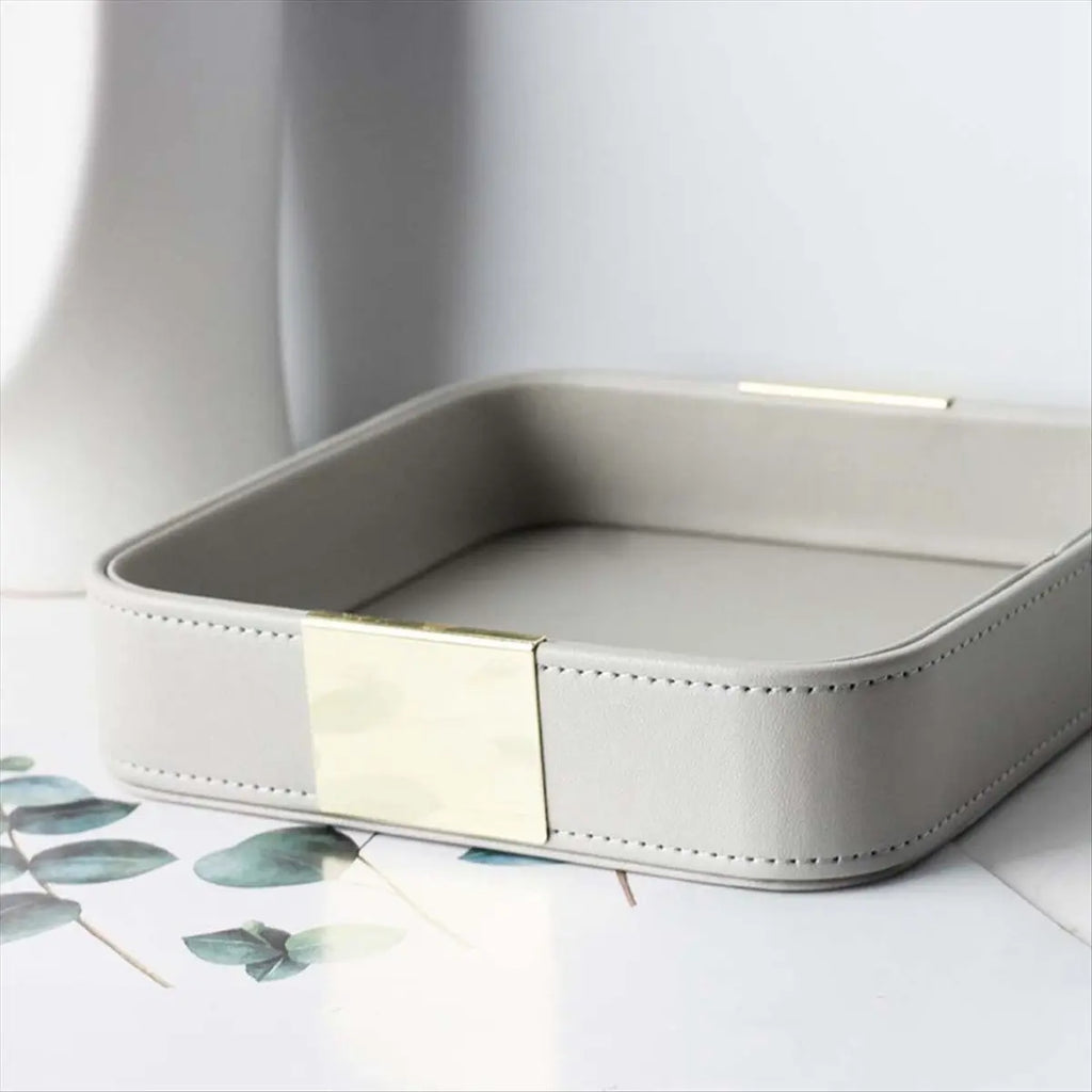Close-up of a square grey PU leather catchall tray with gold accent on a light surface