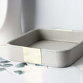 Close-up of a square grey PU leather catchall tray with gold accent on a light surface