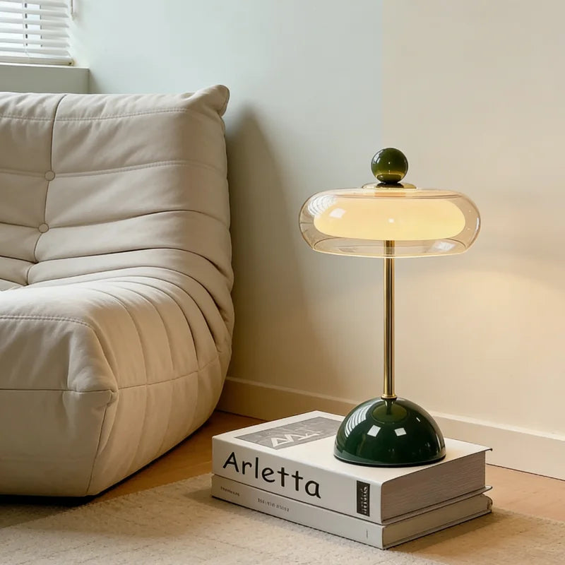 Green mushroom table lamp on book stack beside neutral sofa