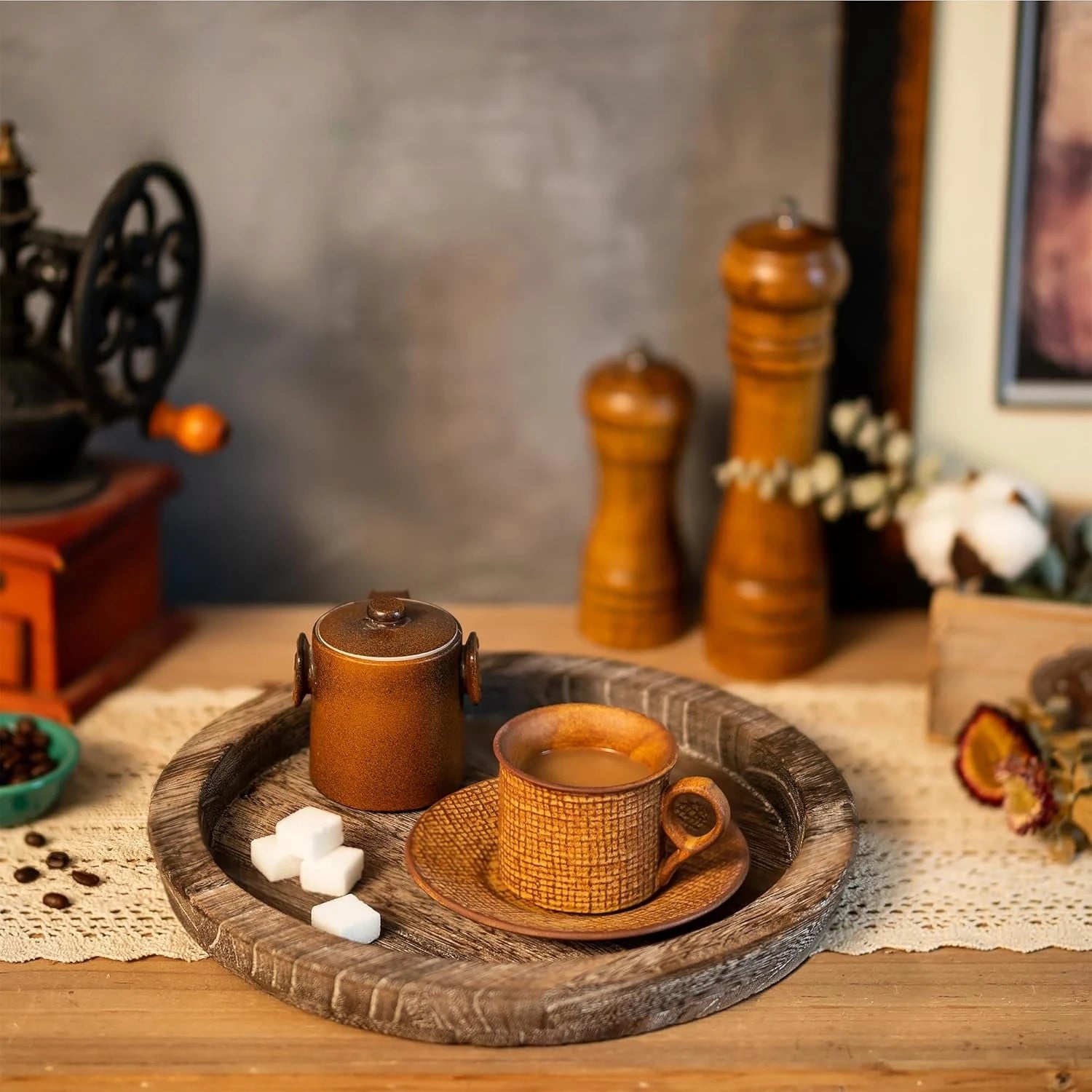 Round rustic wooden tray holding sugar cubes, a cup, and a small canister on a cozy kitchen or dining table