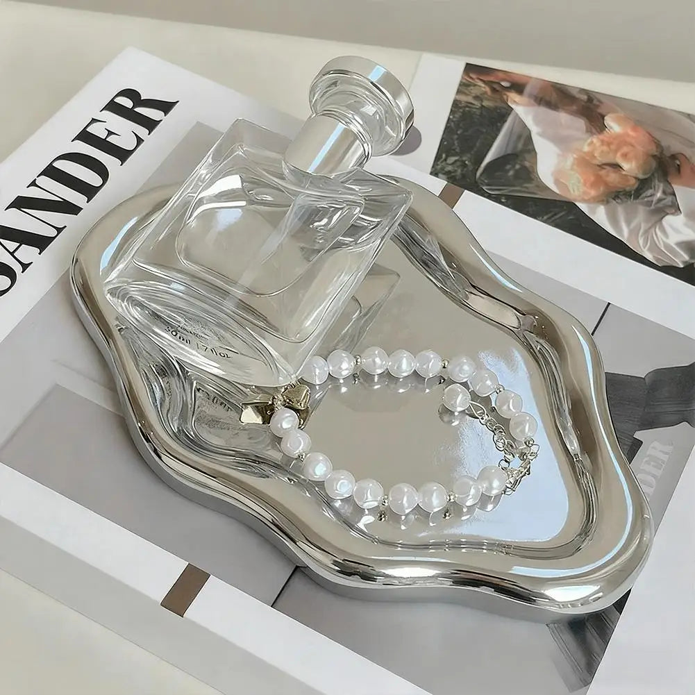 Electroplated silver cloud-shaped tray holding a perfume bottle and pearl bracelet on a magazine