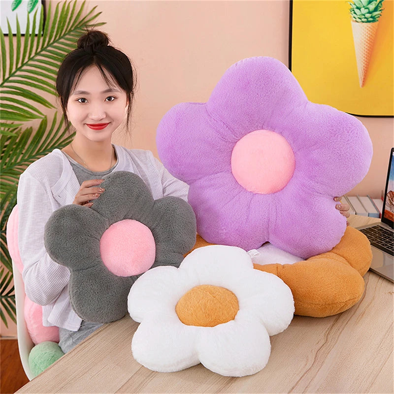 Assorted plush flower cushions in gray, white, purple, and tan on a table with person holding one