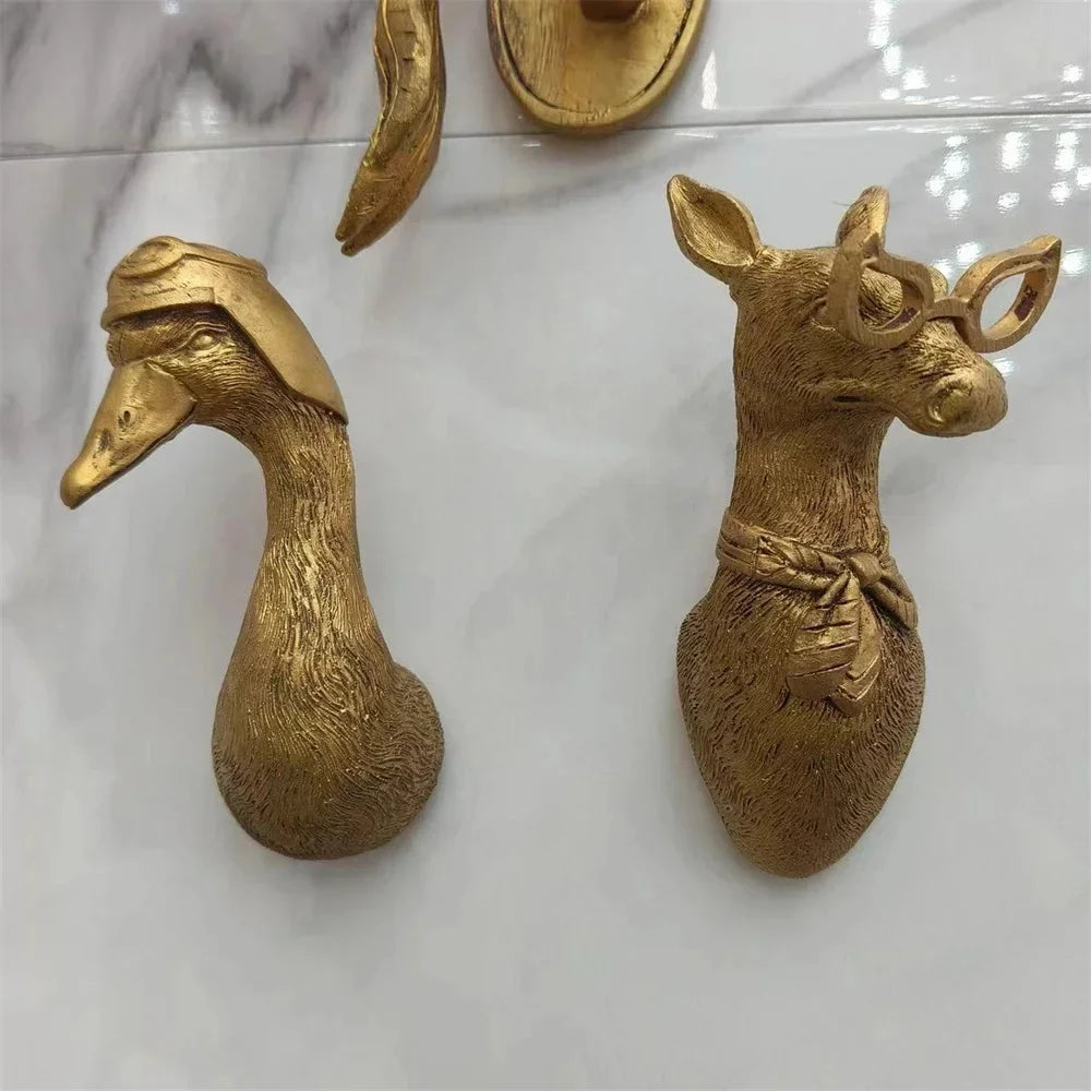 gold duck hook and gold deer hook with glasses next to each other on a marble surface