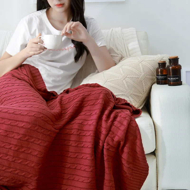 Red cable knit throw blanket over a sofa with a cup of tea