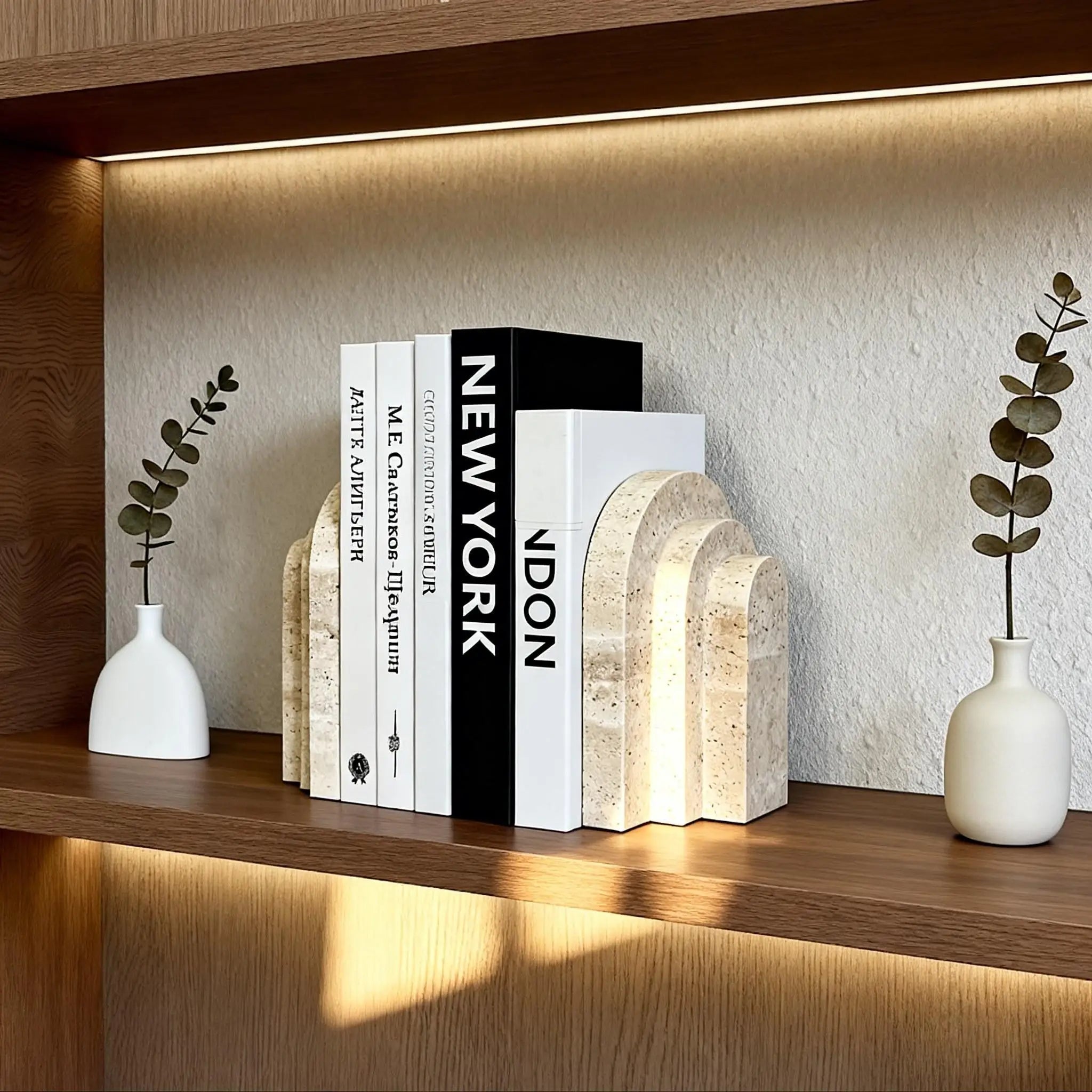 Natural travertine marble bookend with an arch silhouette holding books on a wood shelf, styled with small vases