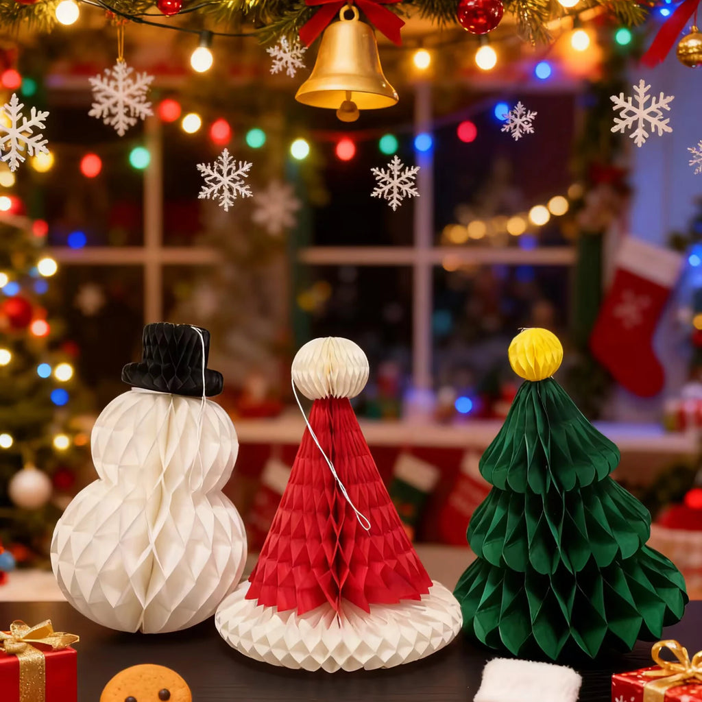 Honeycomb paper snowman, Santa hat, and tree displayed on a Christmas party table with lights and stockings in background