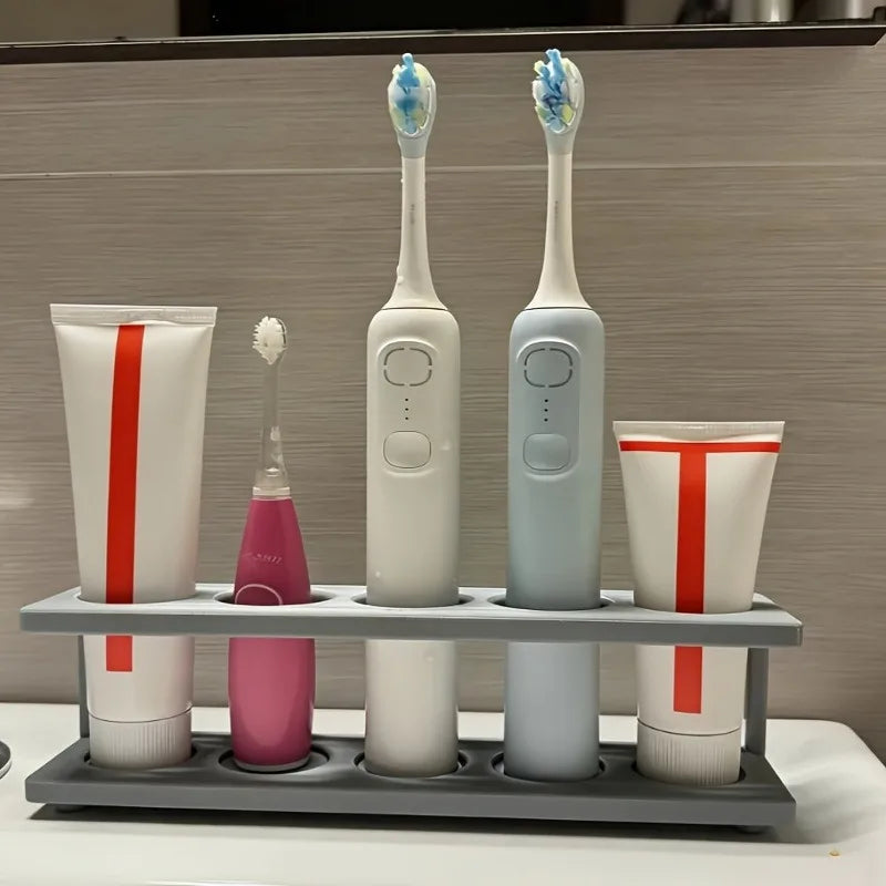 gray plastic multi-slot countertop toothbrush holder storing electric toothbrushes and toothpaste tubes in a modern bathroom