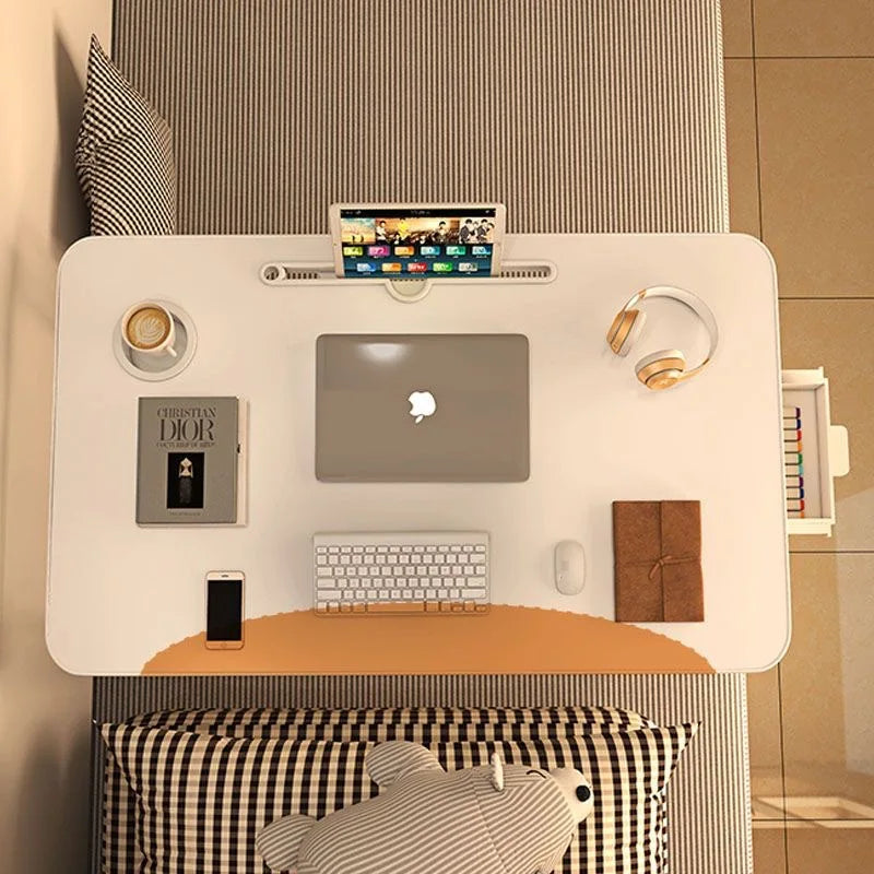 Top-down view of white foldable bedside desk set up with laptop, headphones, cup, and books on a striped bed