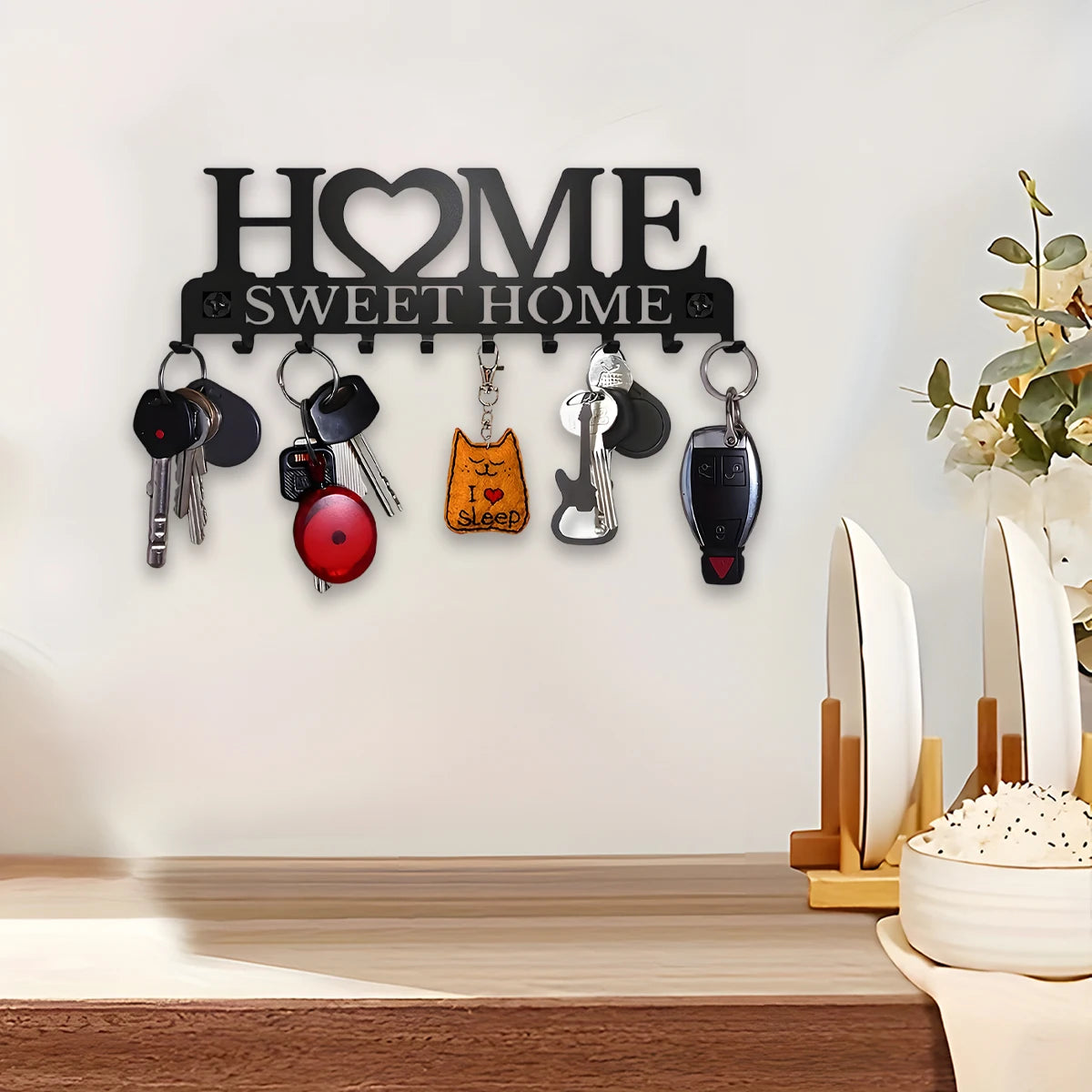 Black metal wall key holder above a kitchen counter, with dishes and decorative flowers nearby.