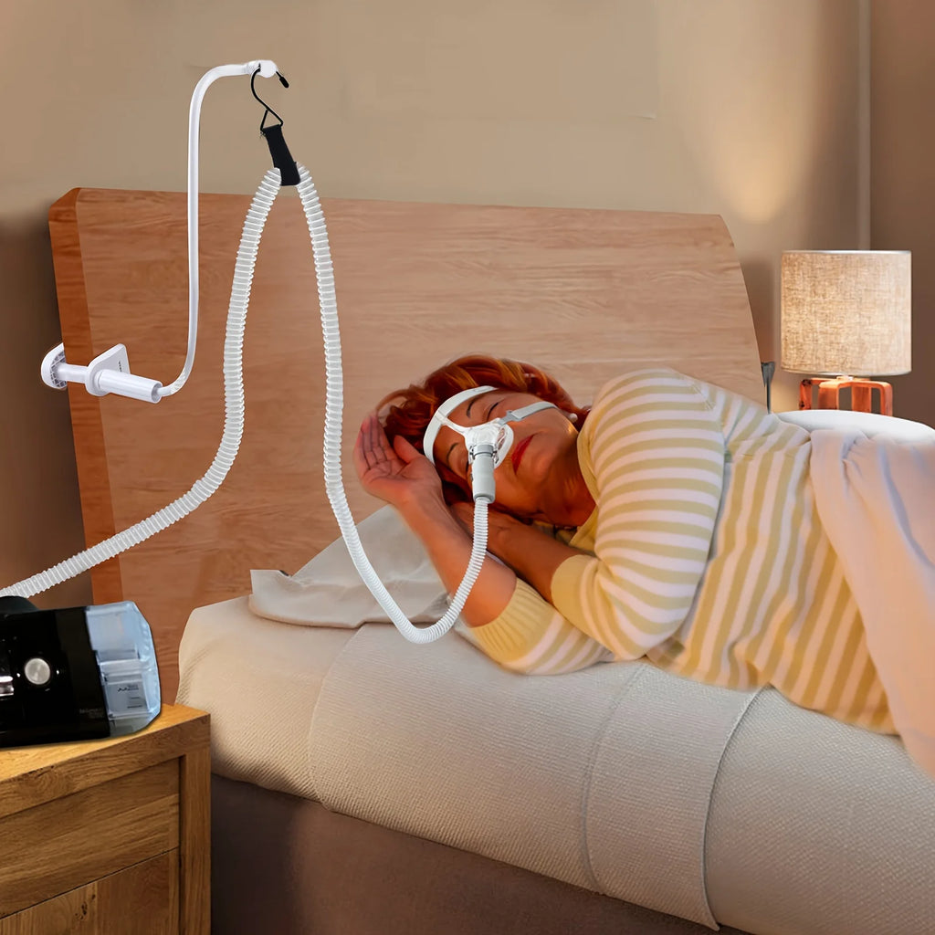Bedside CPAP hose holder clamped to a headboard in a cozy bedroom scene