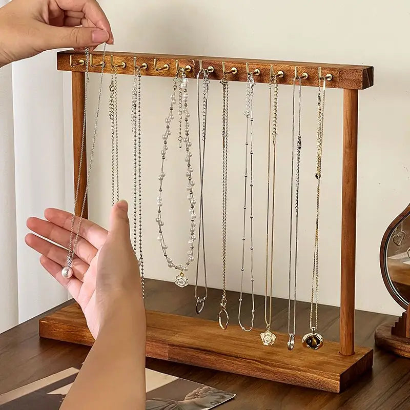 Hand placing a necklace on a solid wood jewelry organizer stand with metal hooks
