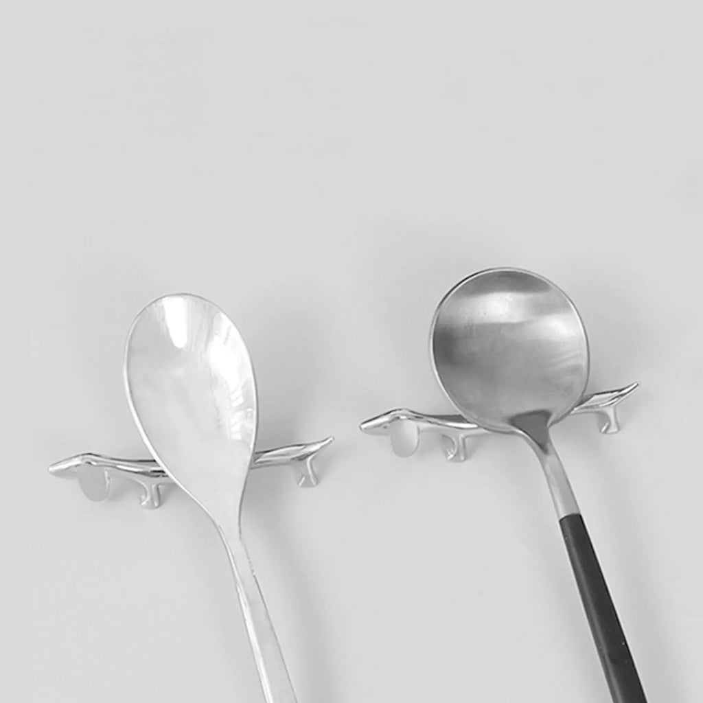 Two silver dog-shaped cutlery rests holding different sized spoons on a table