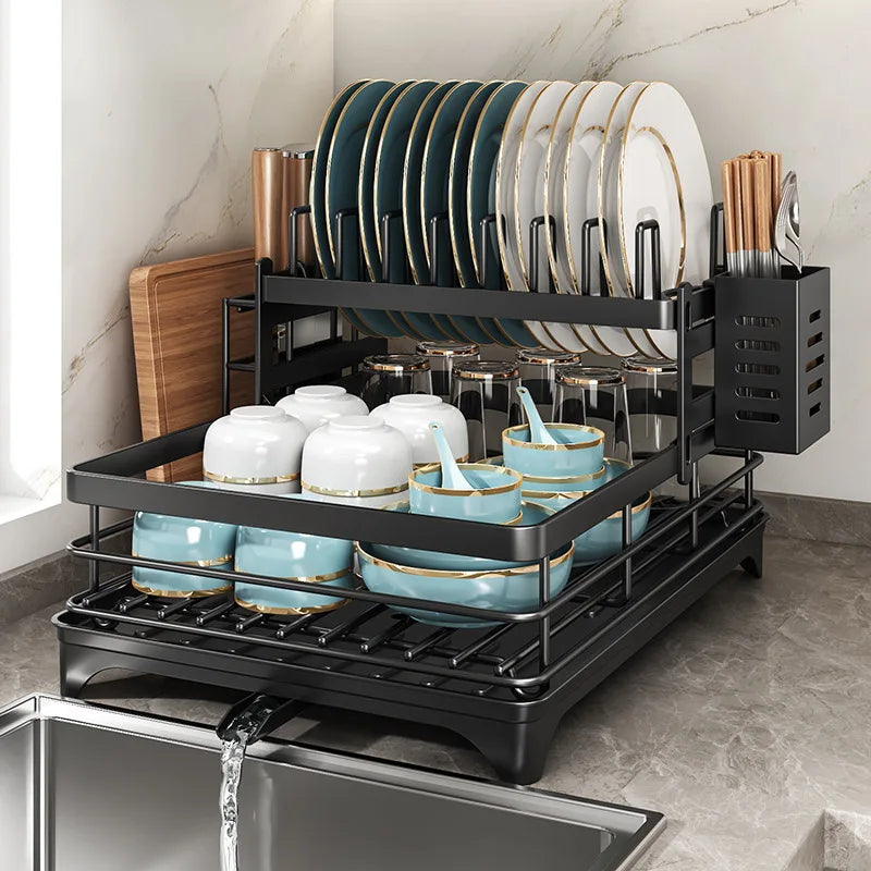 Black 2-tier carbon steel dish drying rack filled with plates, bowls, cups, and utensils on a kitchen counter by the sink