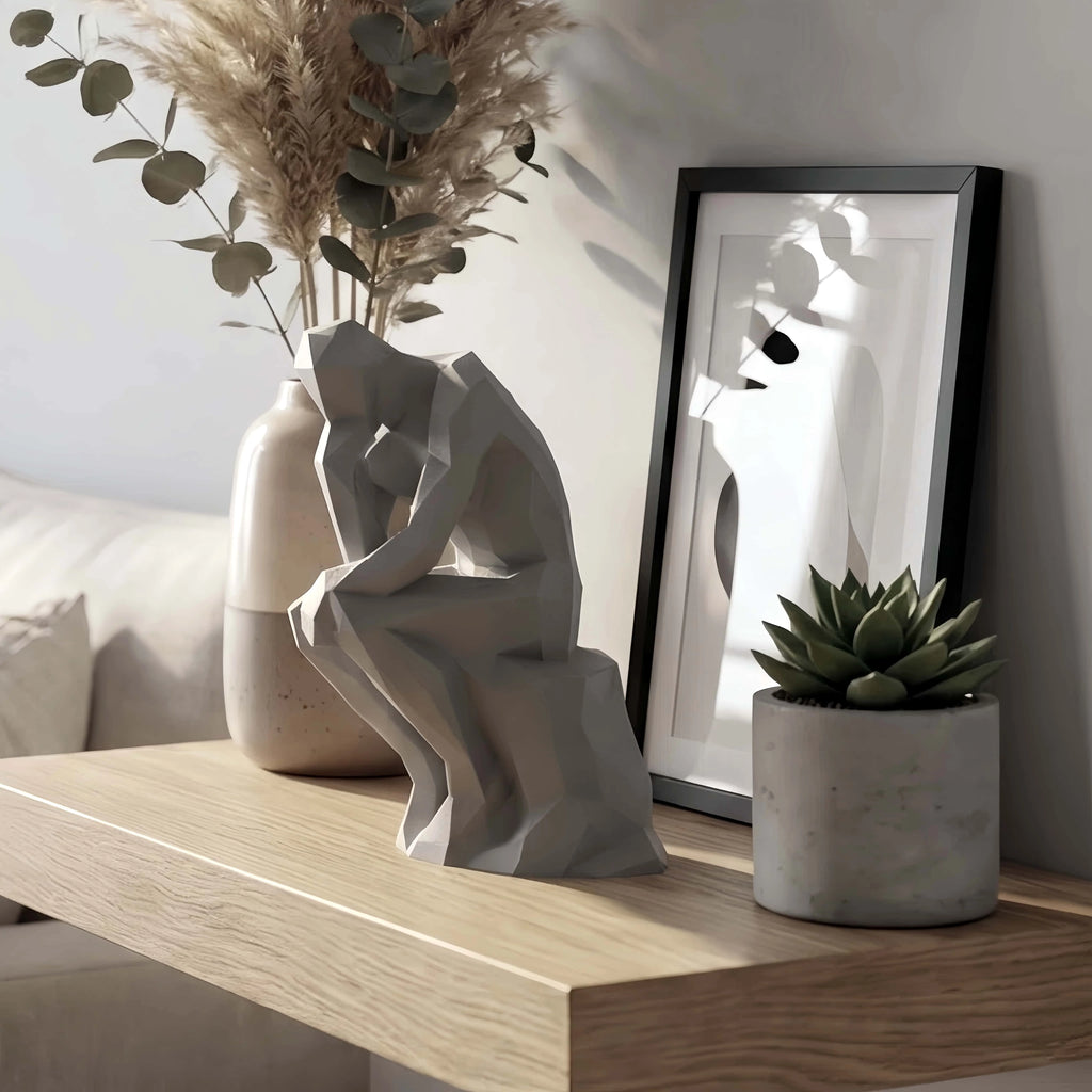 Geometric grey figurine styled on a wooden shelf with vase, art print, and plant in a living room