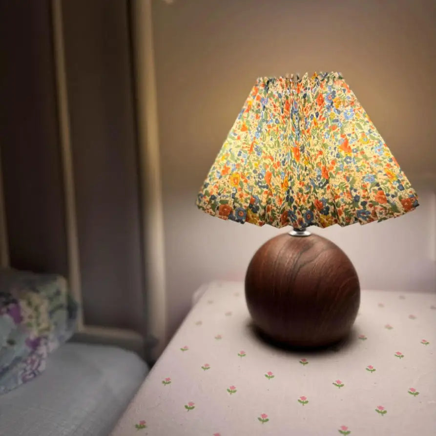 Pleated LED bedside table lamp with round walnut base and floral shade on nightstand