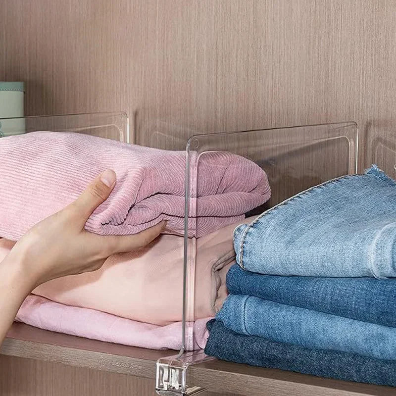 Hand placing folded pink sweater between clear dividers in a closet next to blue jeans