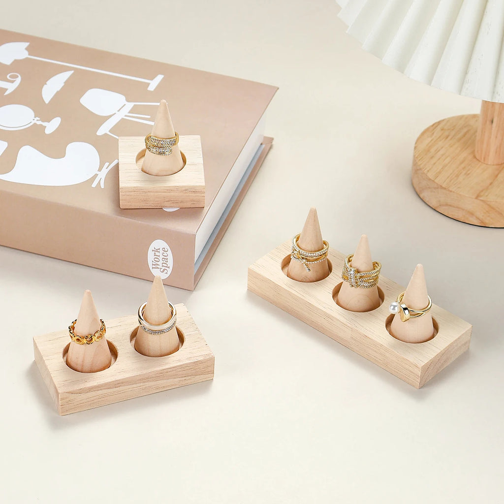 natural wood ring holder stands with gold rings displayed on a desktop beside a lamp and book