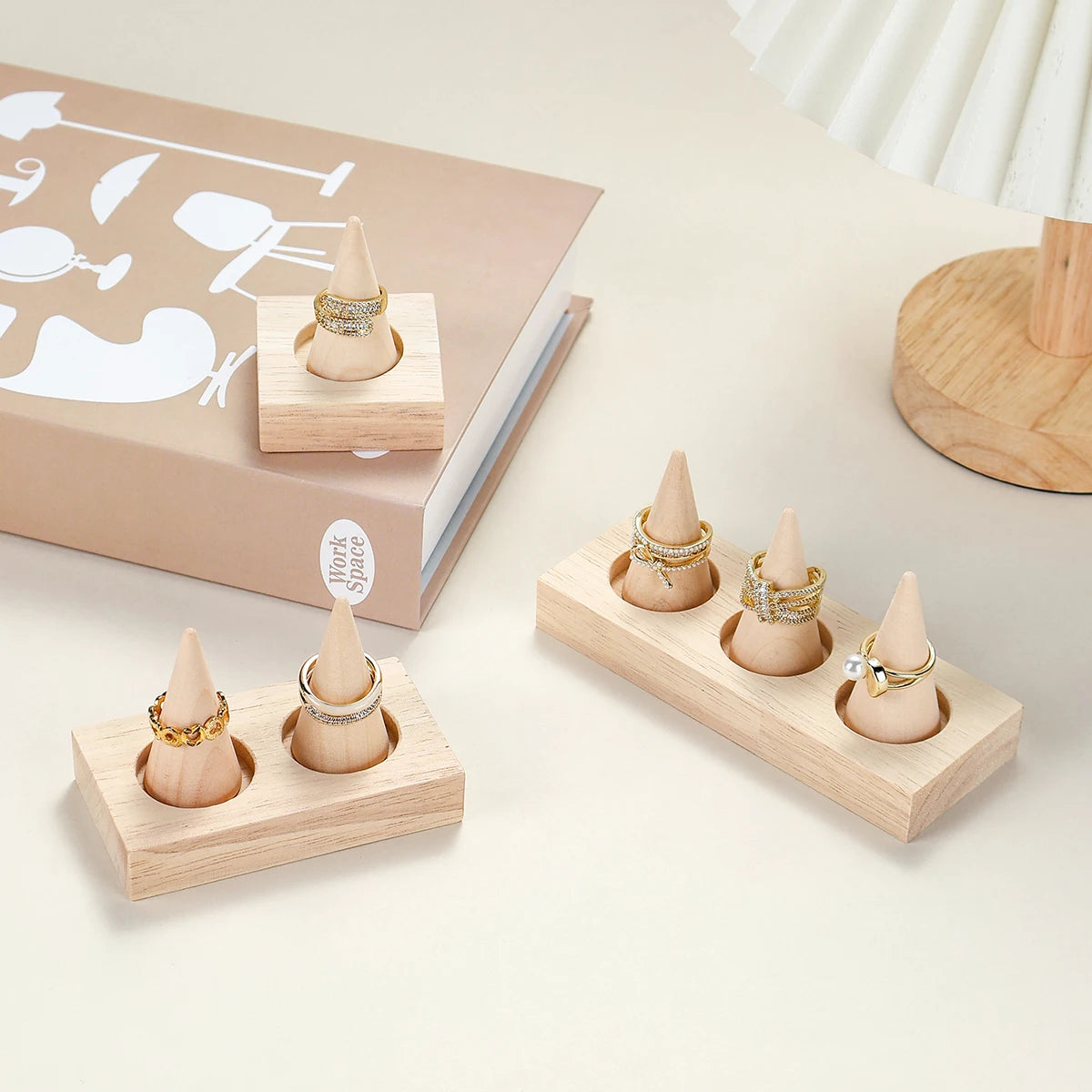 natural wood ring holder stands with gold rings displayed on a desktop beside a lamp and book