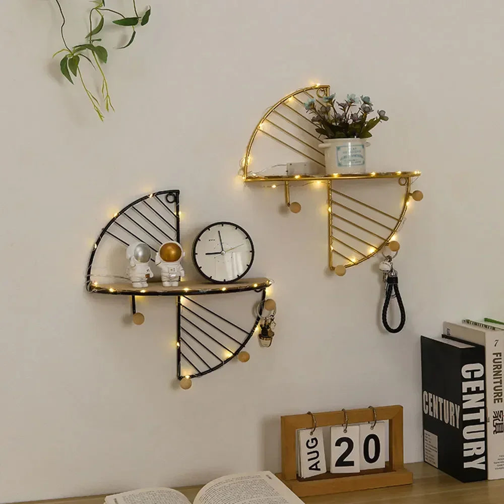 Two metal wall shelves in black and gold, styled with small plants, clocks, and hanging keychains, against a white wall.