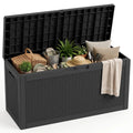 80-gallon black resin rattan deck storage box open and filled with various garden and patio items including plants, cushions, hats, and tableware.