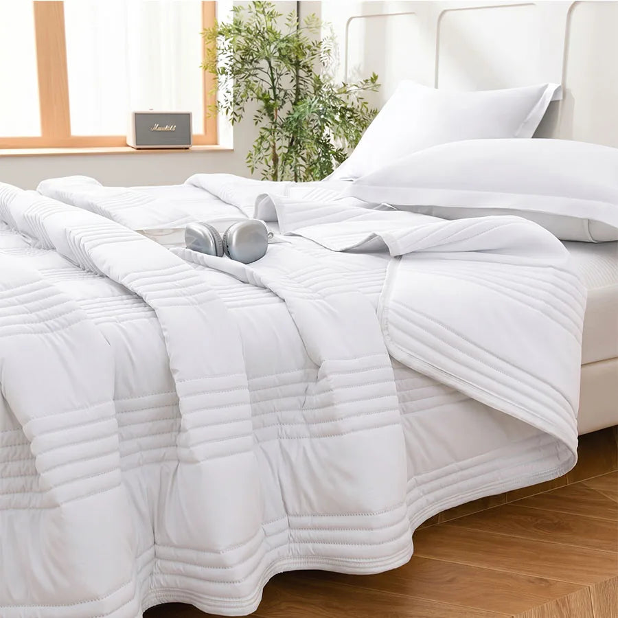 White quilted summer blanket spread on bed with headphones and pillow