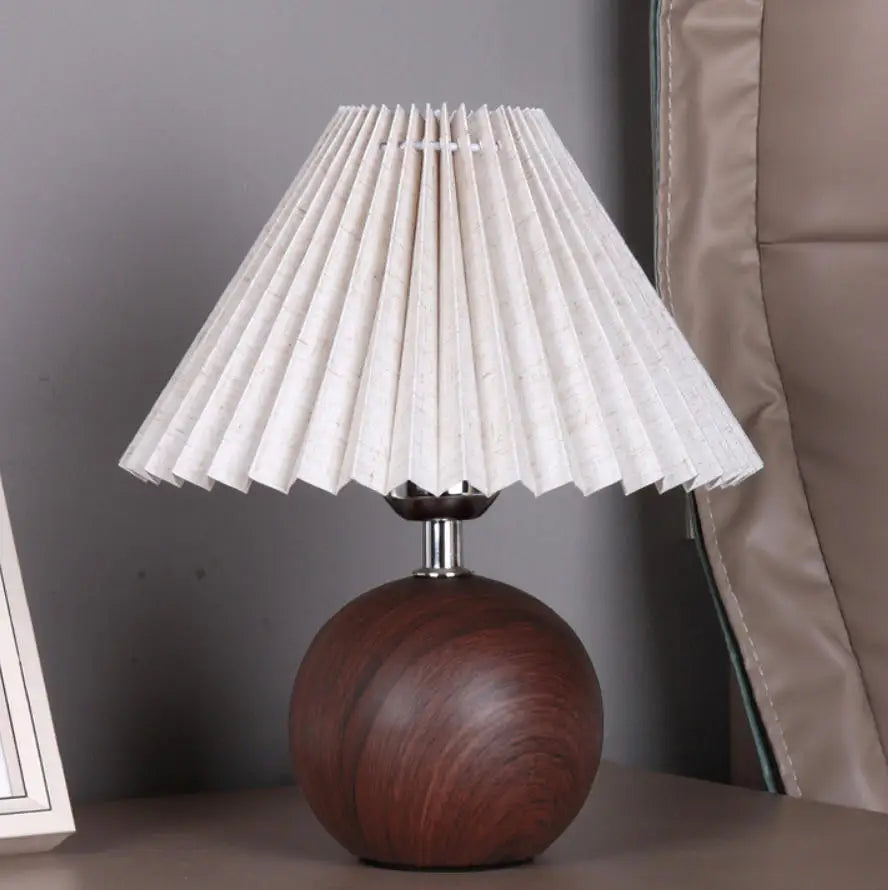 Small table lamp with white pleated shade and walnut-style round base on a bedside table