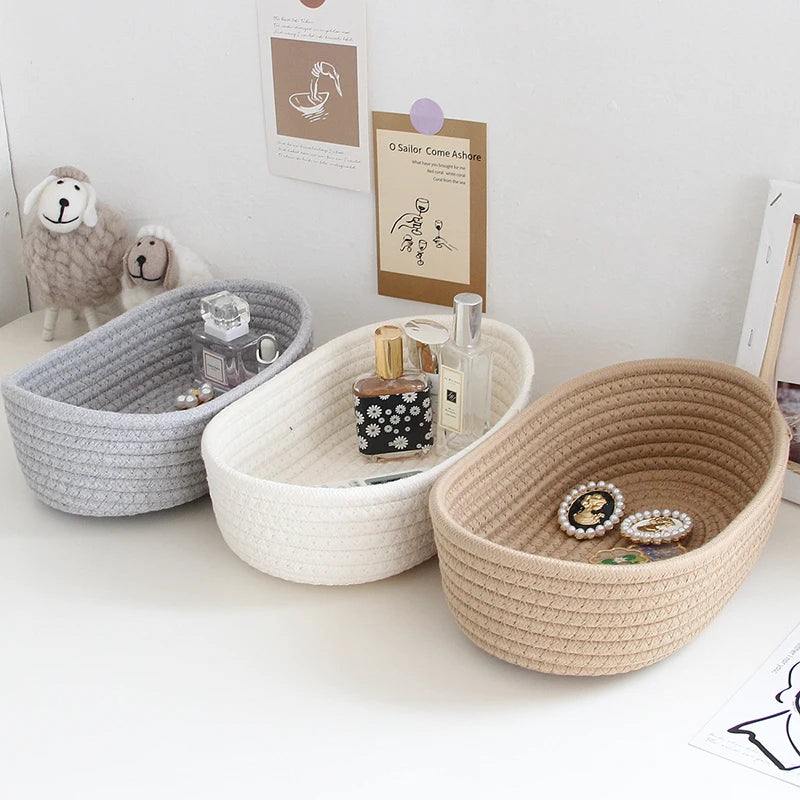 Grey, white, and khaki oval cotton rope storage baskets styled with cosmetics and jewelry on a desk
