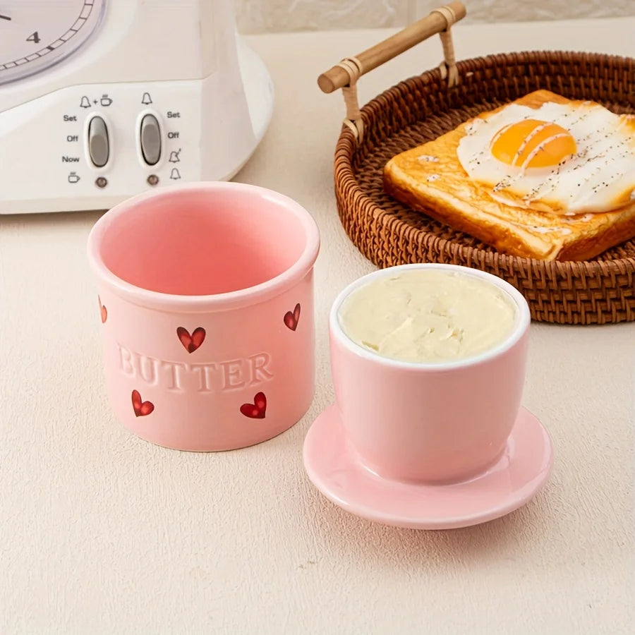 Pink ceramic butter crock disassembled, showing the butter holder insert and heart details, with a breakfast plate nearby.