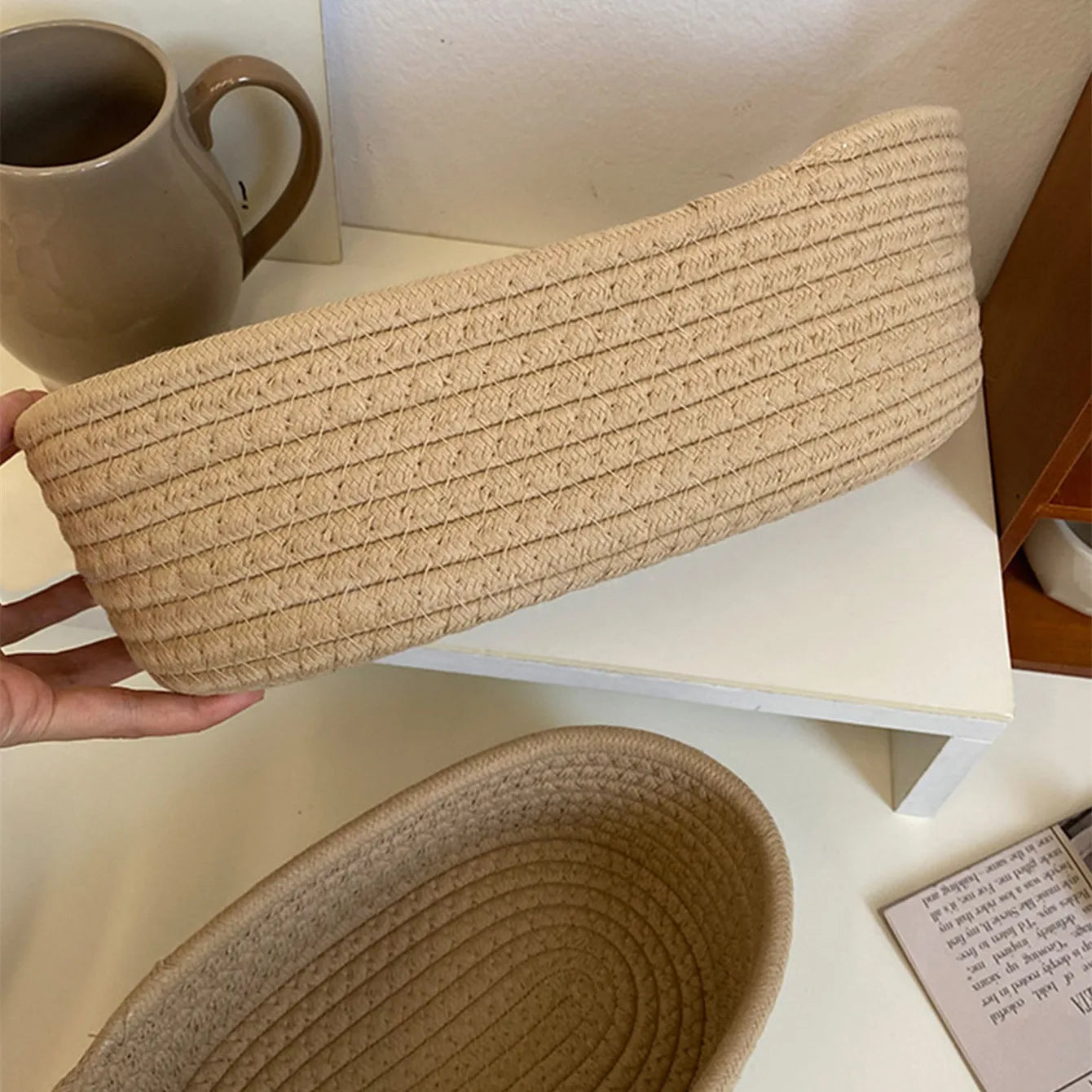 Hand holding khaki oval cotton rope basket to show basket depth and flexibility