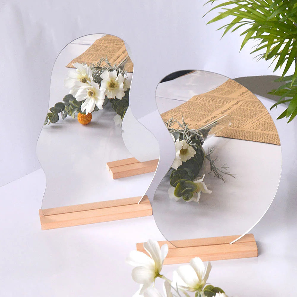 two irregular acrylic mirrors with wooden bases on a white desk