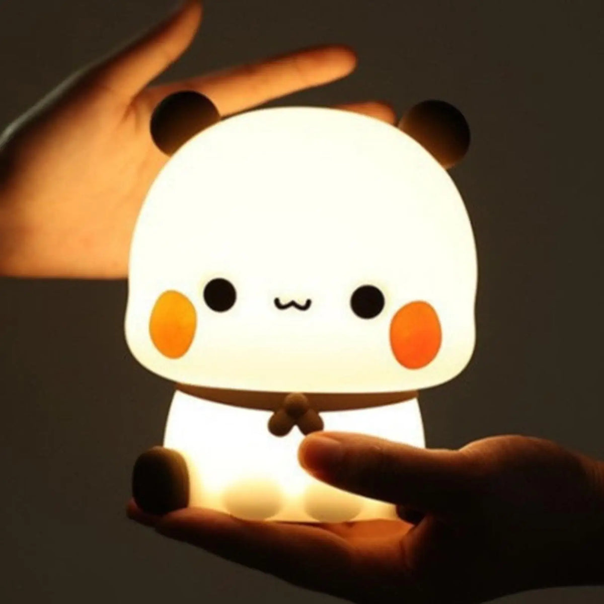 Hands holding a glowing bear silicone night light in a dimly lit room