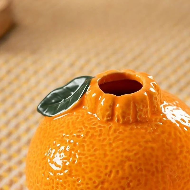 close-up of ceramic orange vase opening with green leaf detail