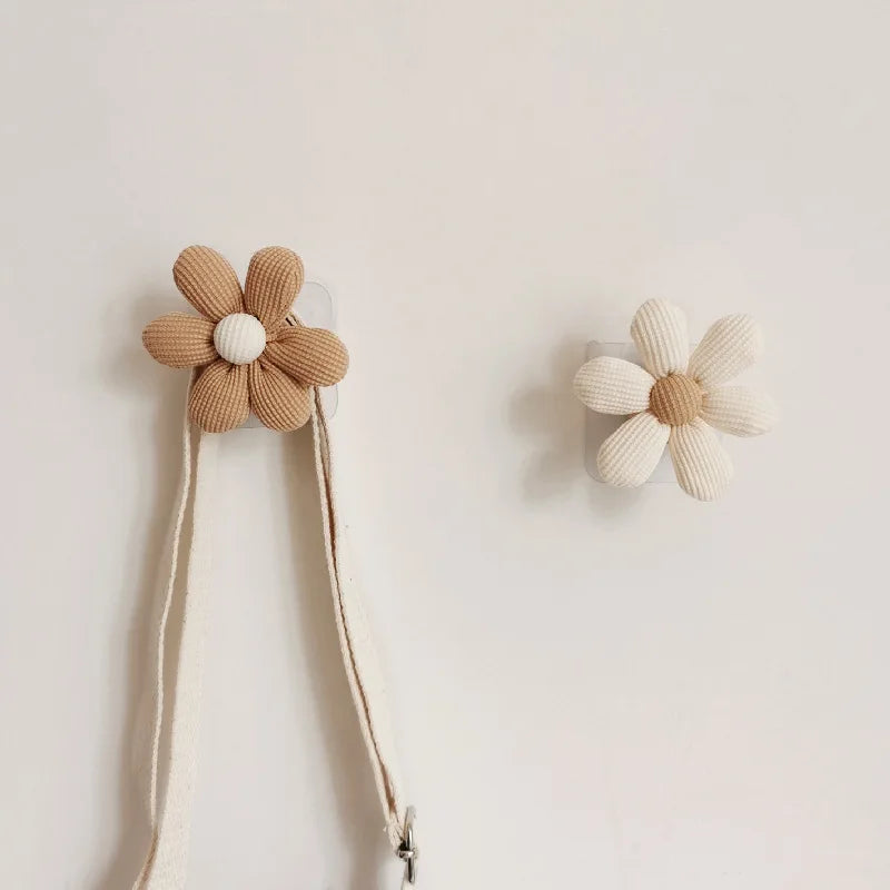 Two daisy-shaped fabric wall hooks mounted on a light wall, both with hanging straps