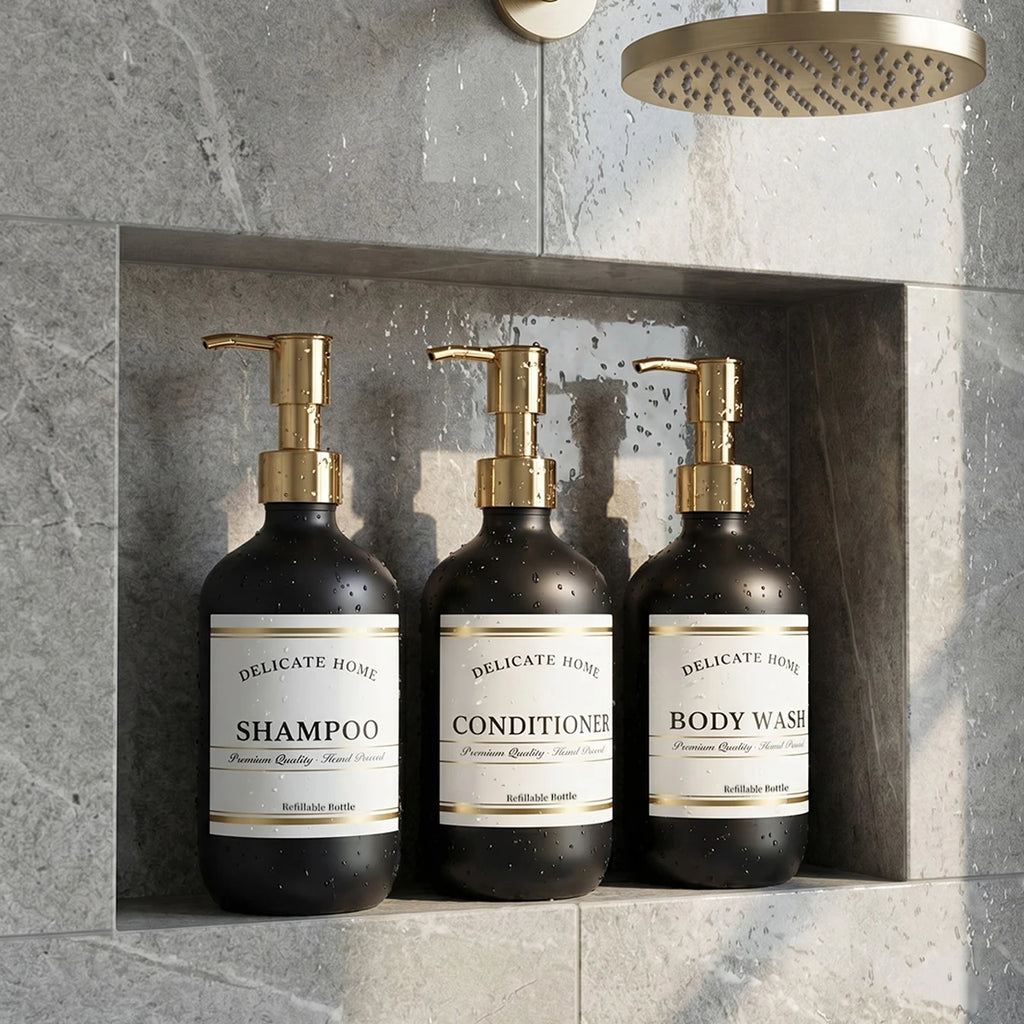 Matte black refillable shower dispensers with gold pumps on a stone shower shelf