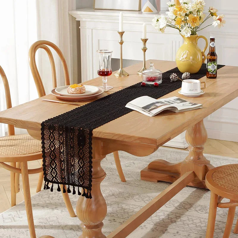 Black lace table runner with tassels across a light wood dining table, dining room scene