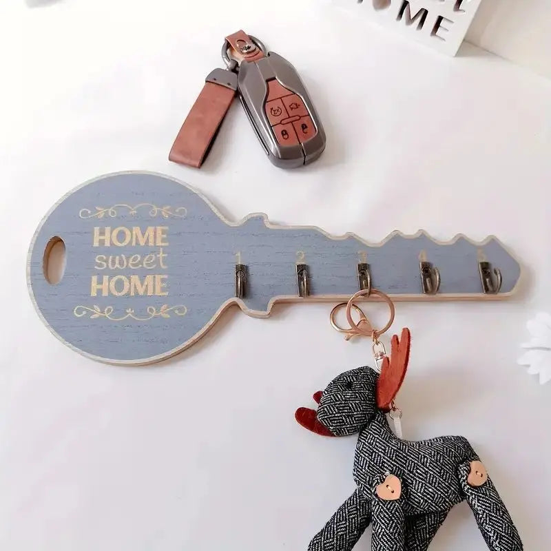 White wood key-shaped wall key rack with 5 hooks, shown on a white surface with a set of keys and a stuffed animal keychain
