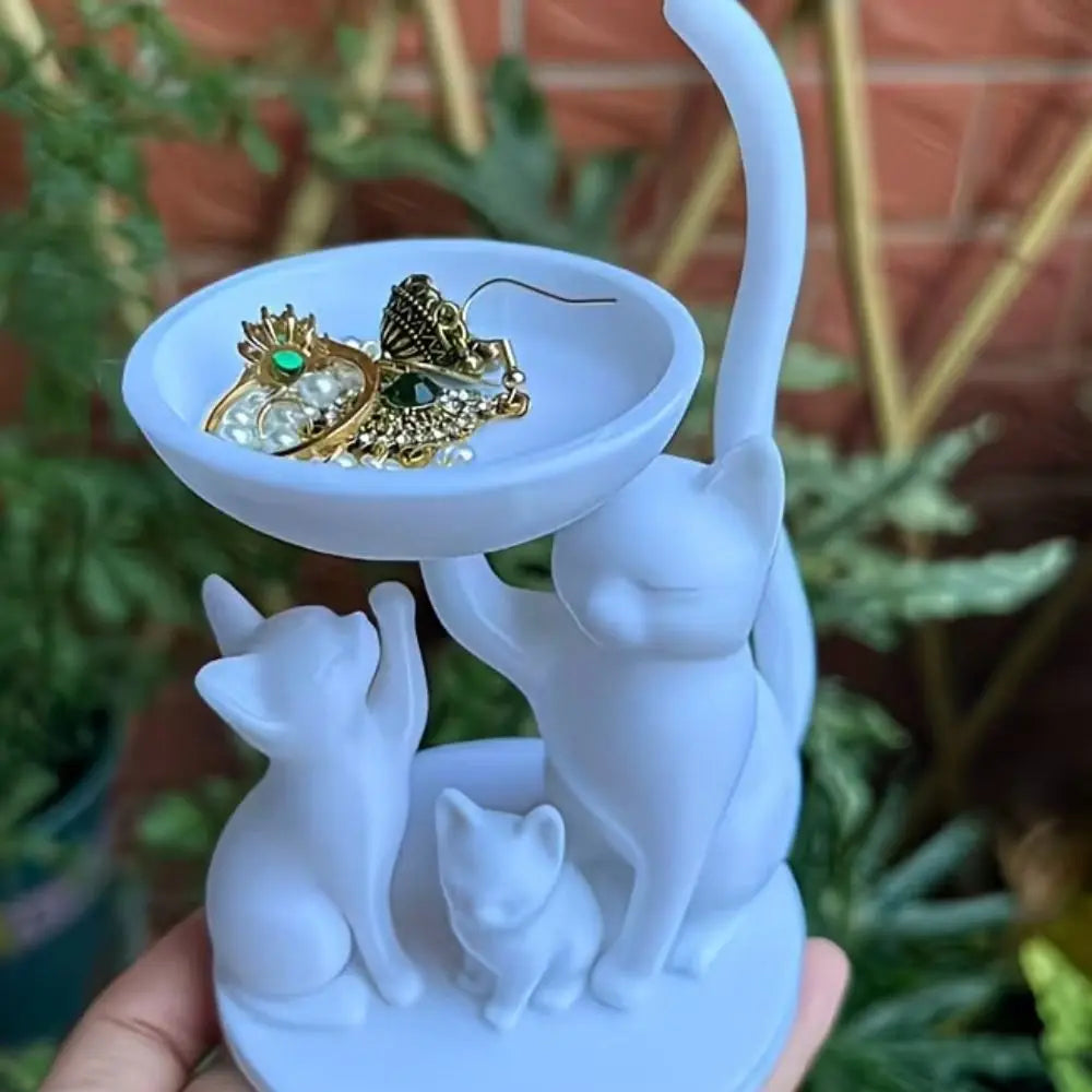 White cat family jewelry tray held in hand with earrings and rings inside