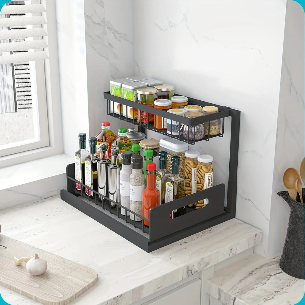Black two-tier pull-out metal organizer on a marble kitchen counter, organized with spice jars, bottles, and pantry items