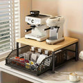 Kitchen counter coffee organizer station with wooden top shelf holding two coffee machines and a metal pull-out basket below storing coffee pods and supplies