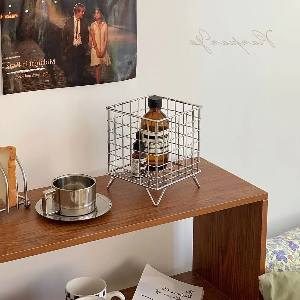 Silver metal storage basket on a wooden shelf holding bottles and decor