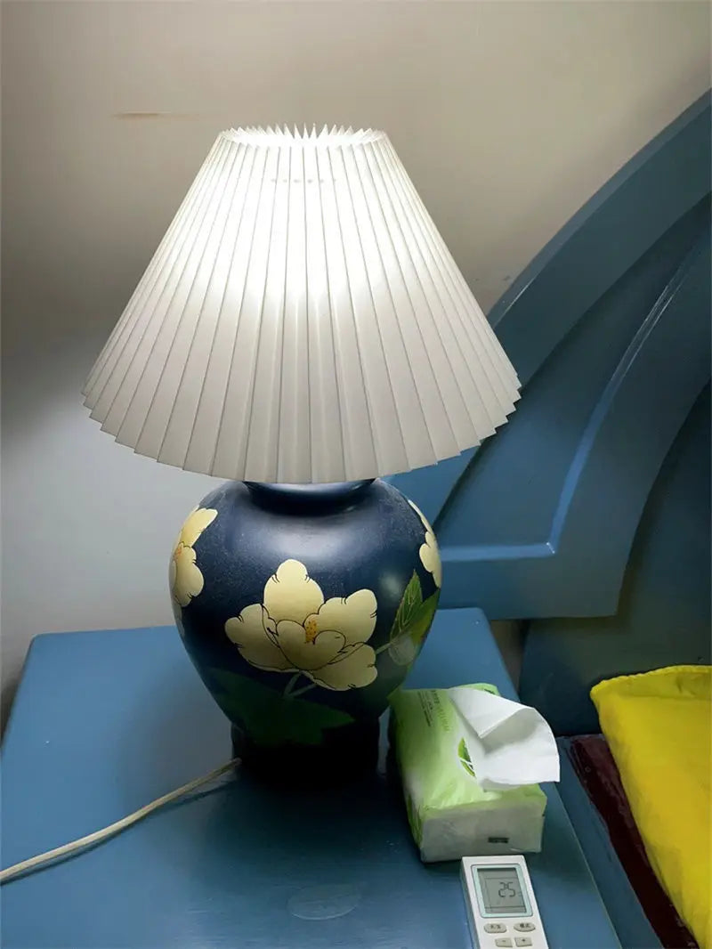 White pleated lampshade on floral ceramic table lamp in bedroom setting