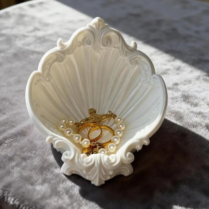 Shell shaped white jewelry dish with accessories on a sunlit velvet surface