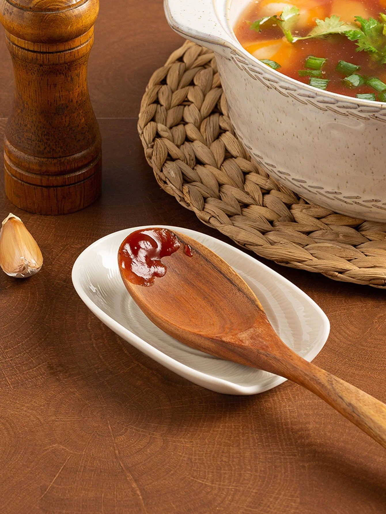 White ceramic spoon rest on a wood counter with a wooden spoon and soup bowl nearby