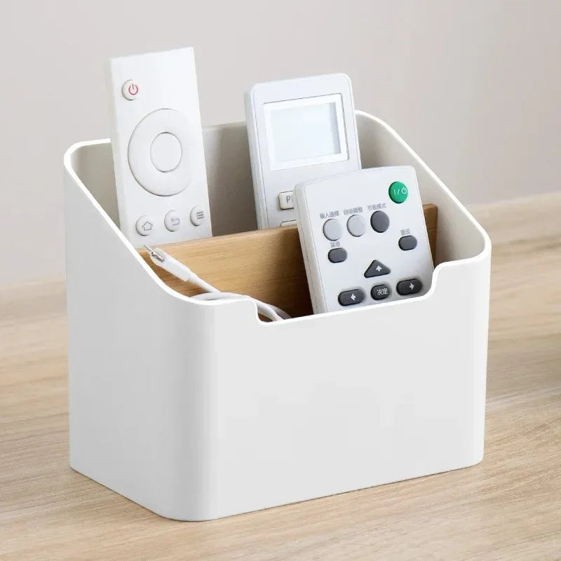 White plastic and wood divider storage box on a tabletop holding three remote controls.