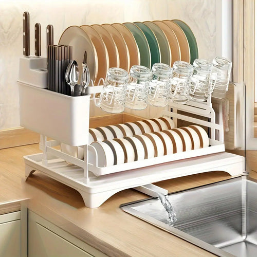 White 2-tier dish drying rack with plates, bowls, cups, and cutlery placed on a kitchen counter with water draining into a sink